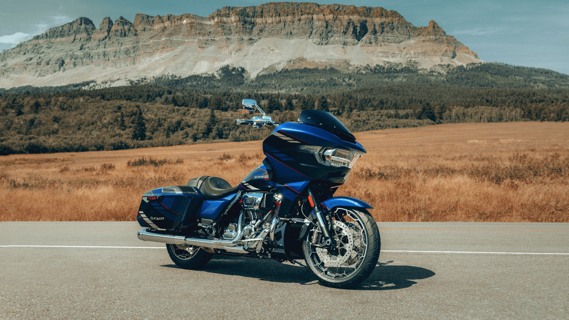2025 Harley-Davidson CVO Road Glide in striking blue, parked on open road with mountains backdrop.