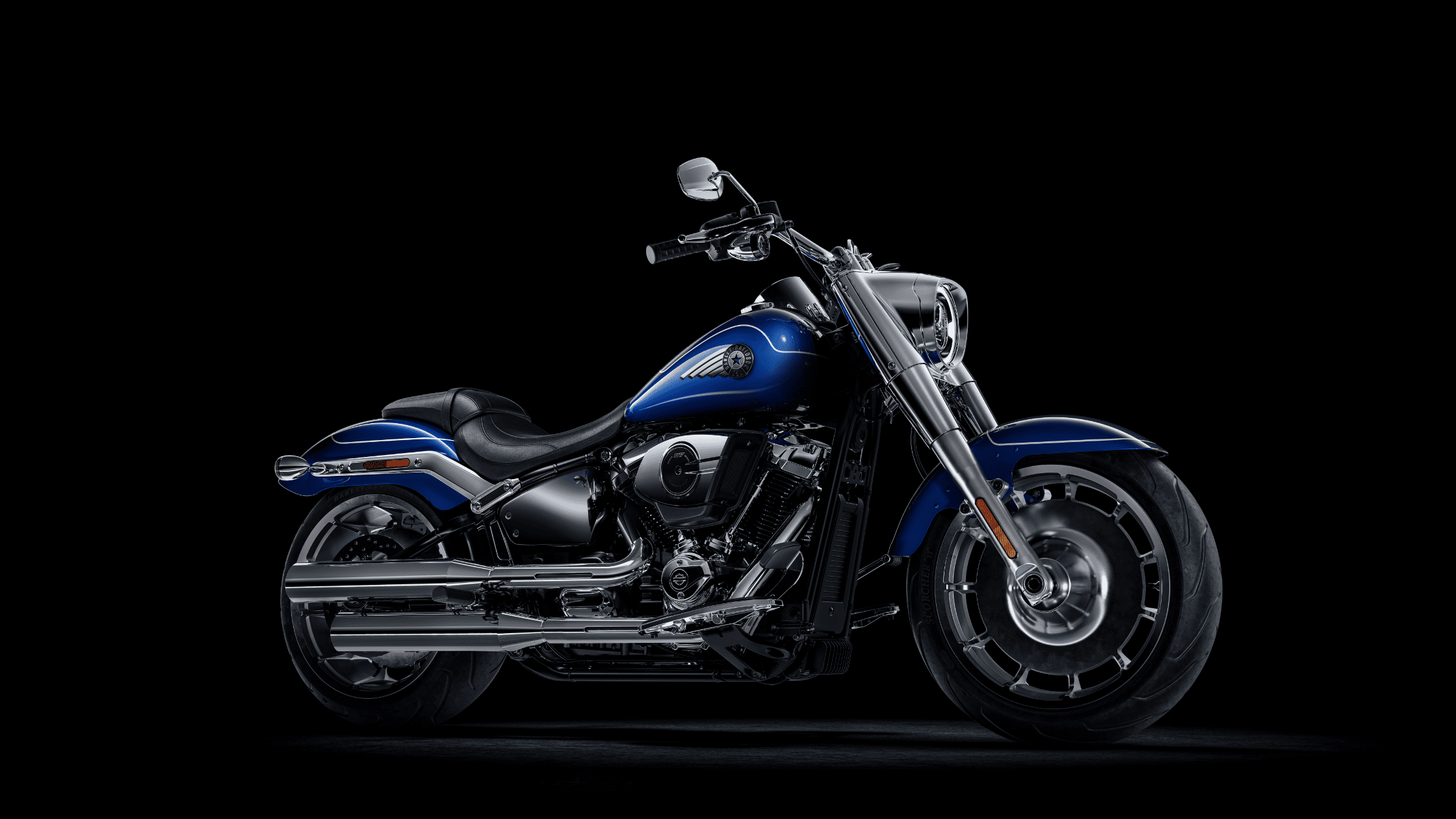 Studio shot of a 2025 Harley-Davidson Fat Boy in blue and chrome, showcasing its solid disc wheels and wide stance on a black background.