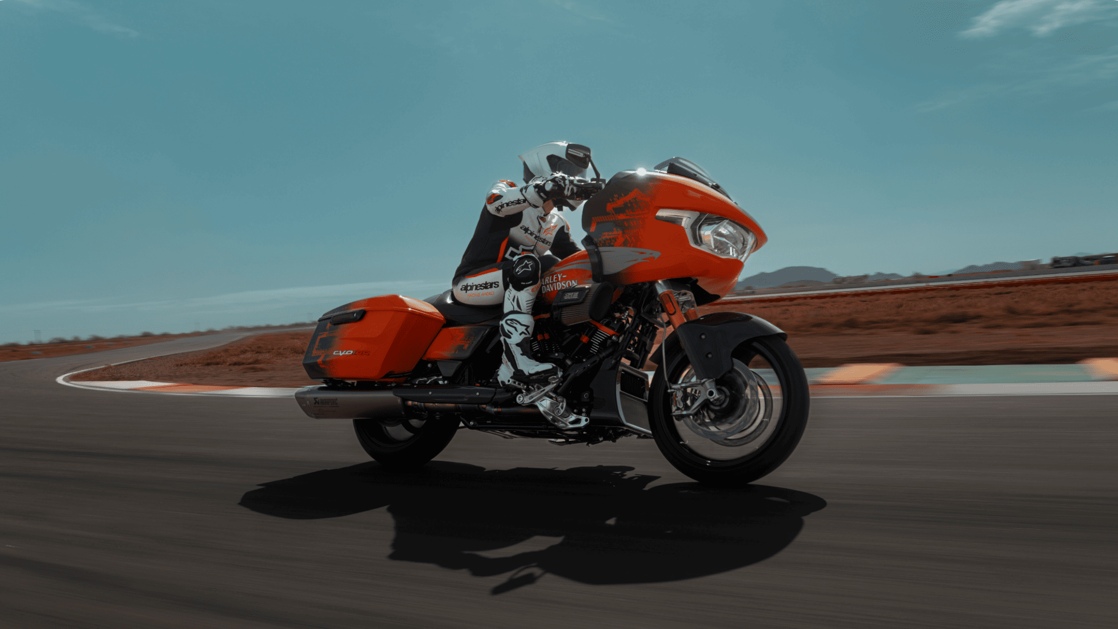 A rider leans into a turn on the 2025 Harley-Davidson® CVO™ Road Glide® RR in bright orange on a racetrack.