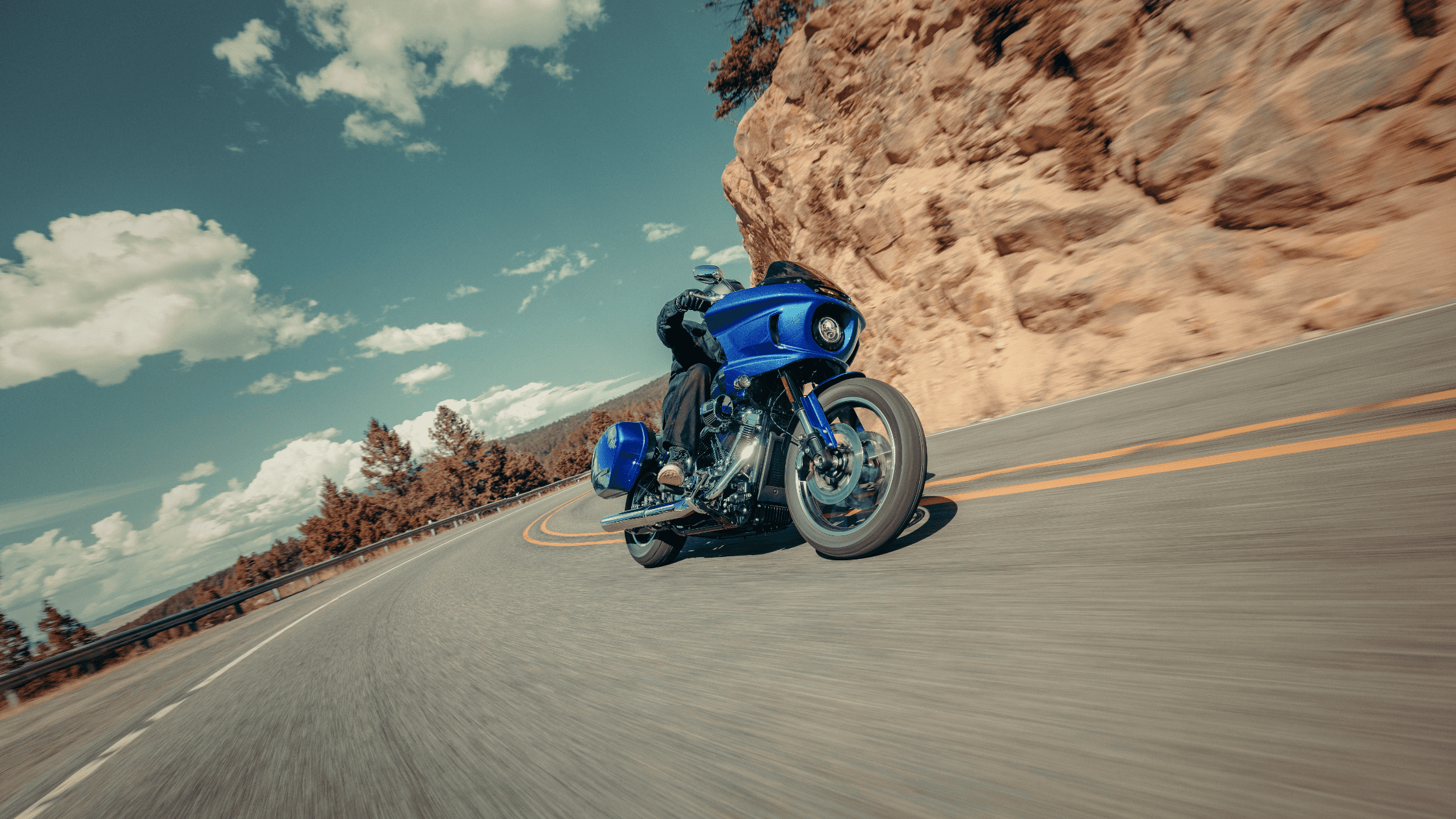 2025 Harley-Davidson® Low Rider® ST in vivid blue leaning into a canyon curve, showing aggressive fairing, saddlebags, and performance stance.