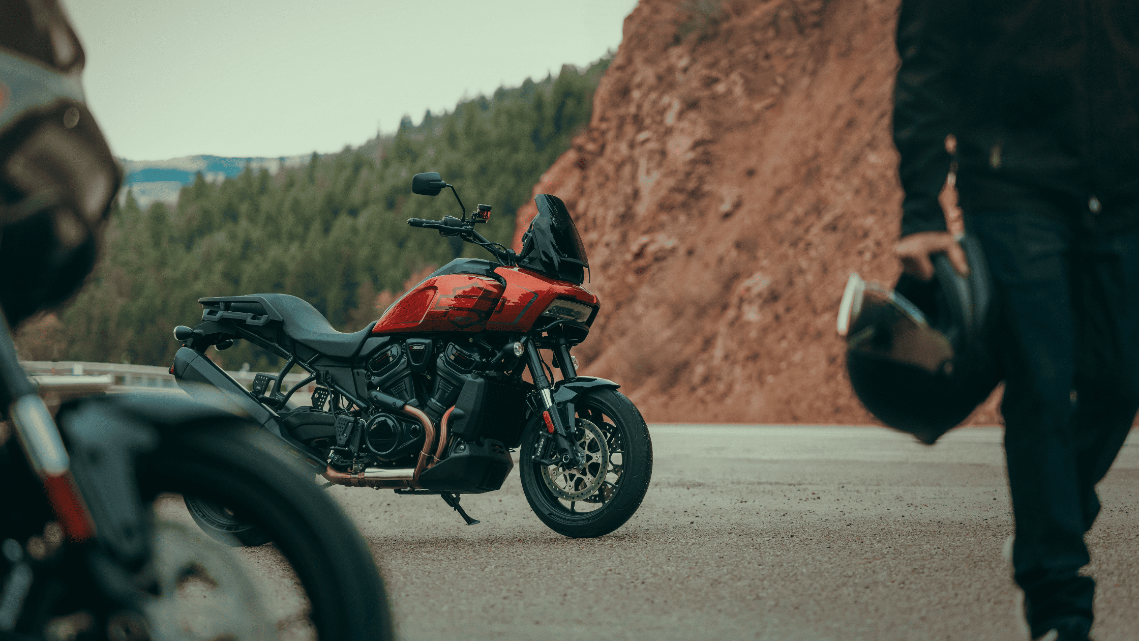 2025 Pan America 1250 ST parked on a mountain road with rider walking nearby holding a helmet.