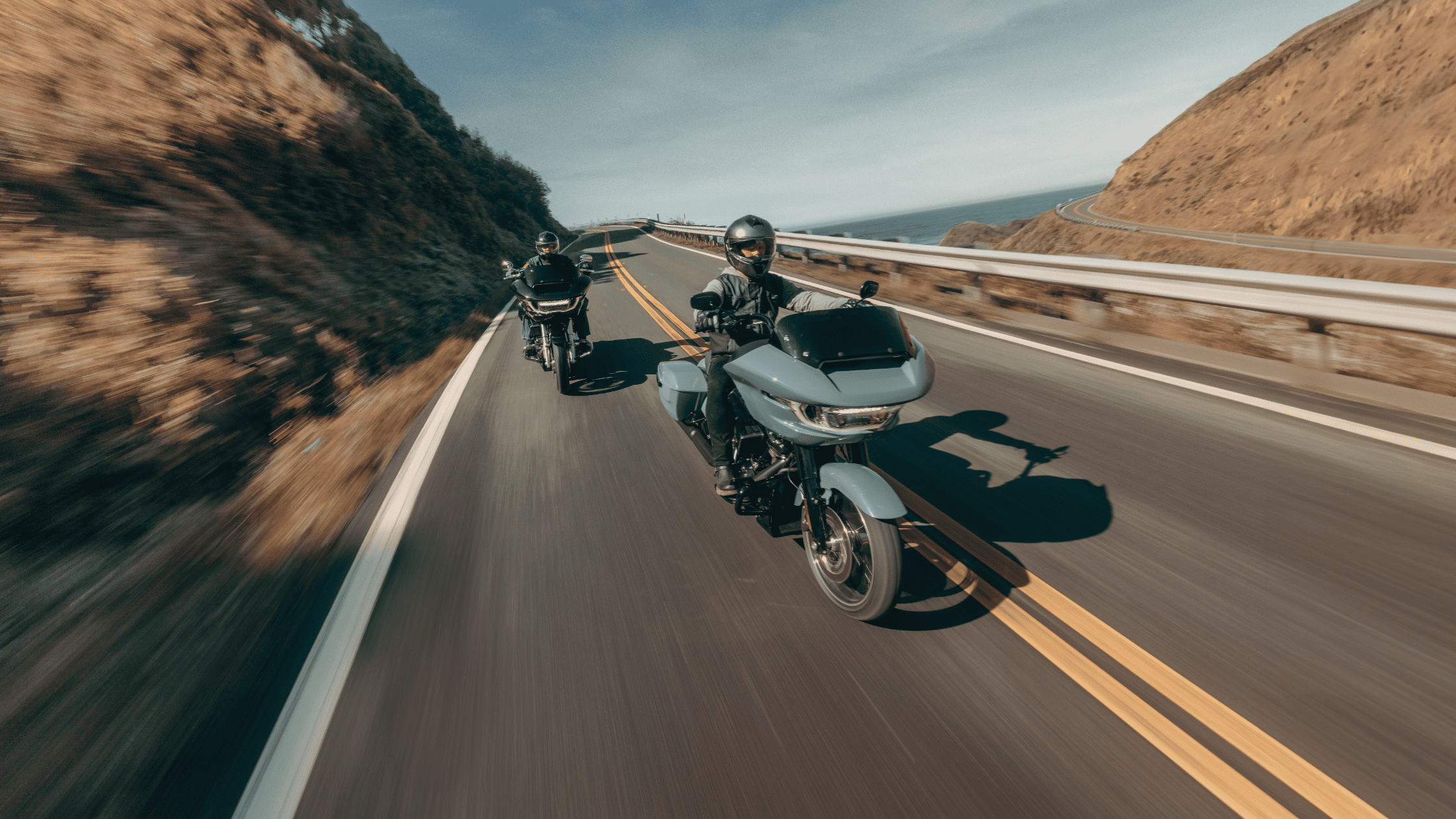 2025 Harley-Davidson® Road Glide® riding on a coastal highway with touring fairing and saddlebags.