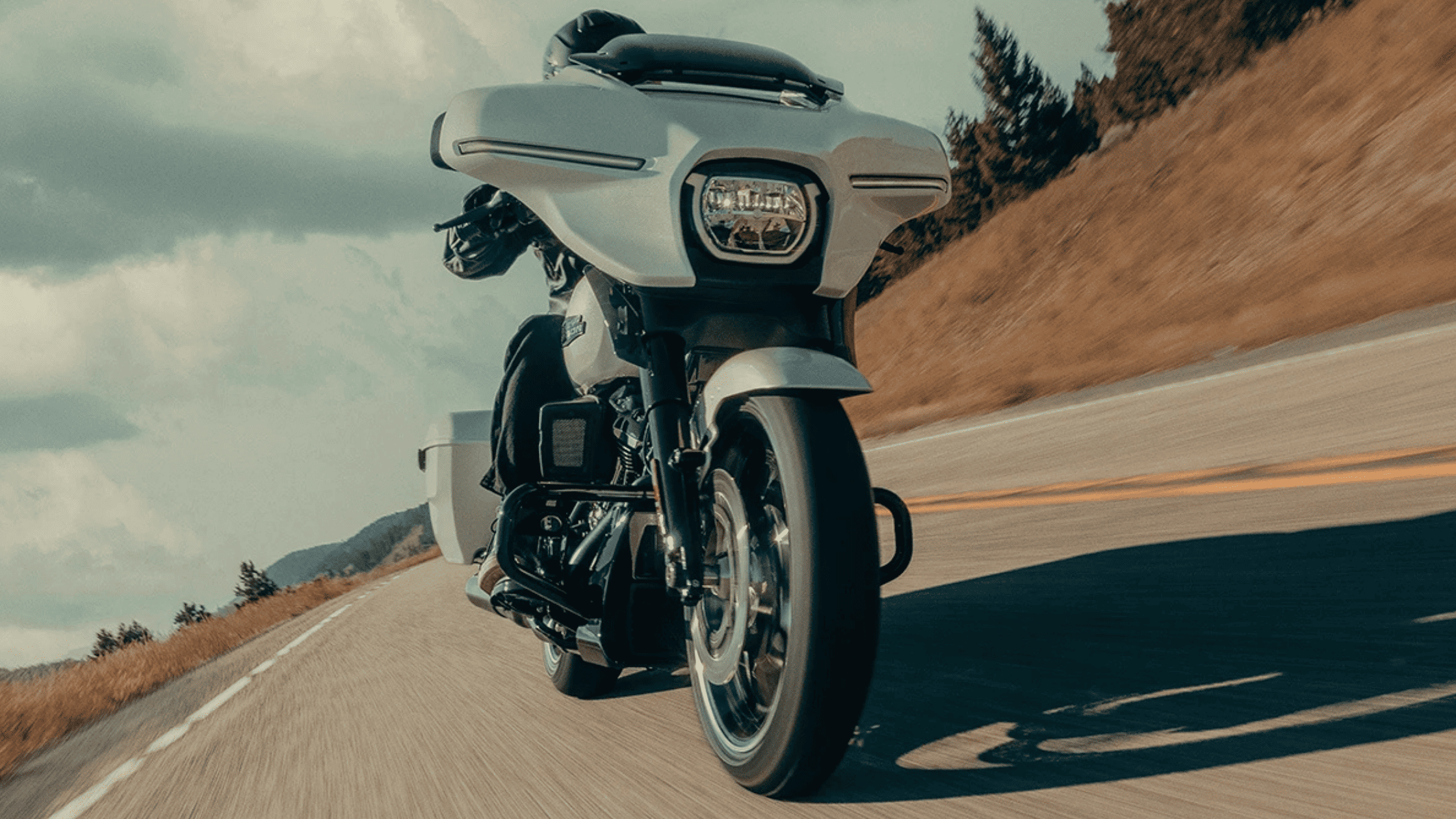 Rider on a 2025 Harley-Davidson Street Glide cruising on a winding mountain road under a cloudy sky.
