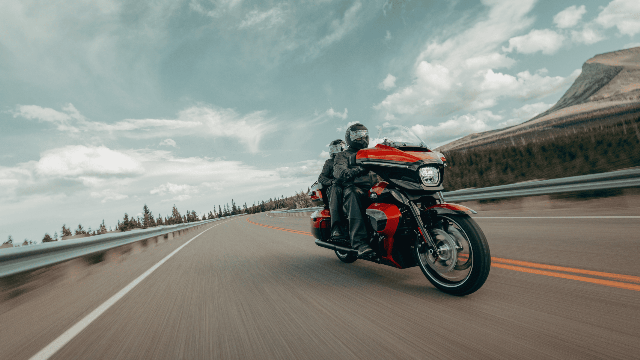 2025 Harley-Davidson Street Glide® Ultra in red and black, two-up riding on a mountain highway with full gear.