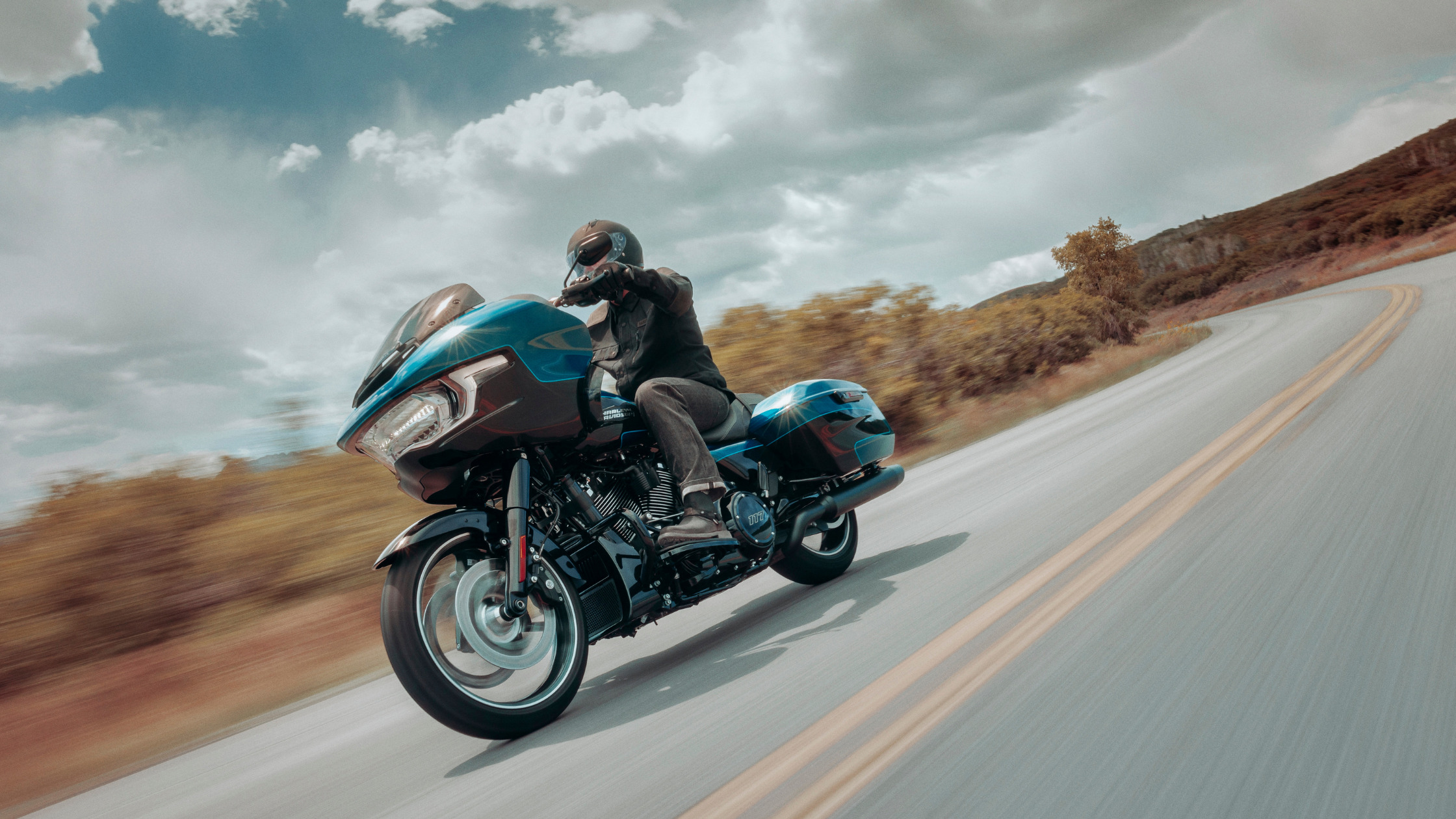2026 Harley-Davidson® Road Glide® touring motorcycle riding on winding highway, front three quarter action view.