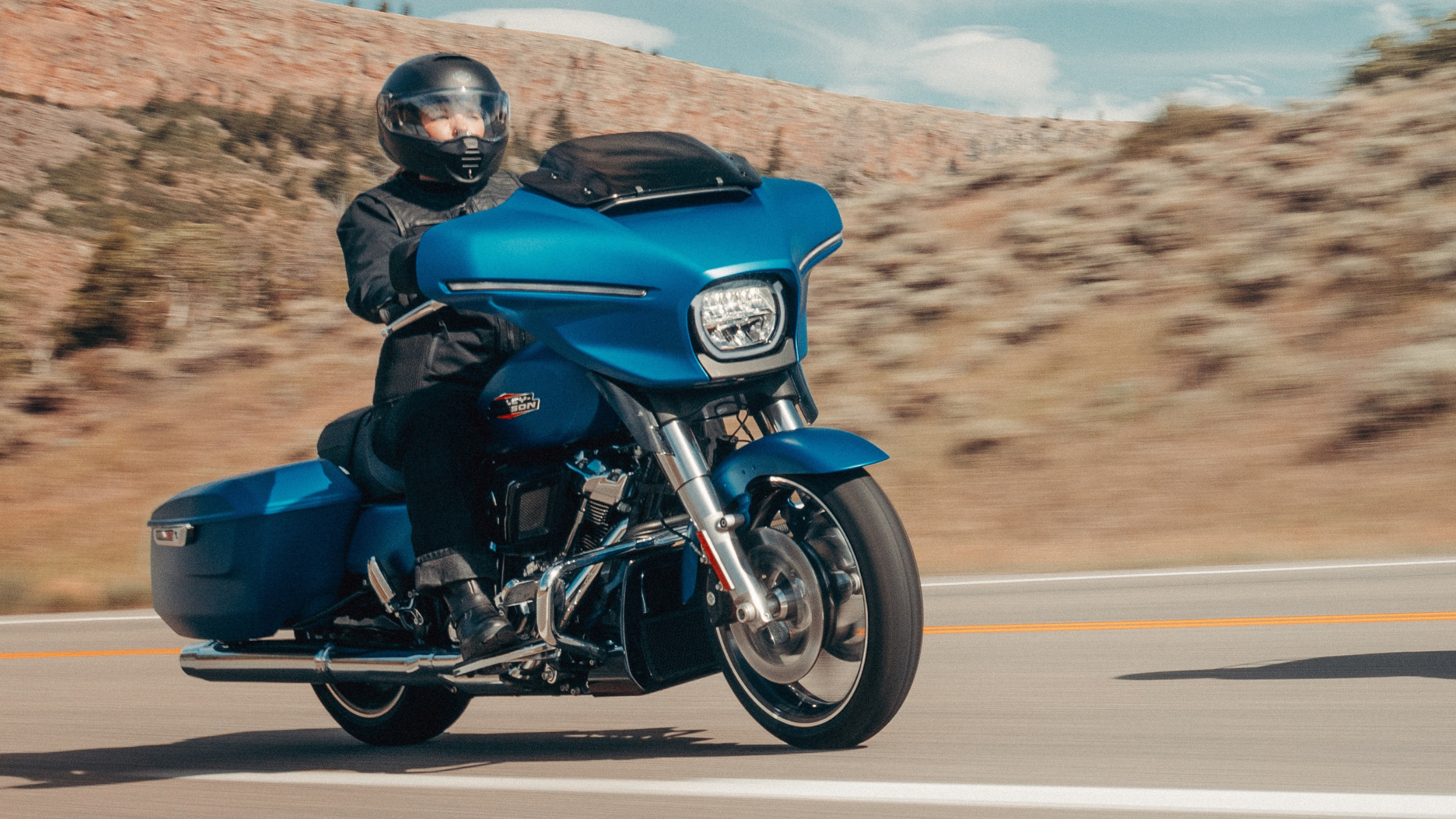 2026 Harley-Davidson® Street Glide® in blue riding on open road, front three quarter exterior action view.